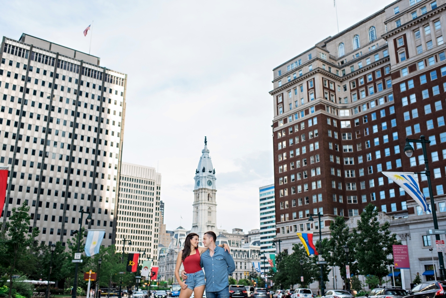 An engaged couple standing in front of love park with city hall in the background.